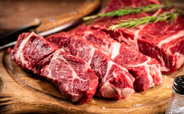 Raw beef on a cutting board with rosemary and spices.