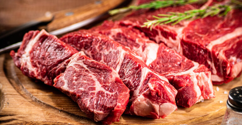 Raw beef on a cutting board with rosemary and spices.